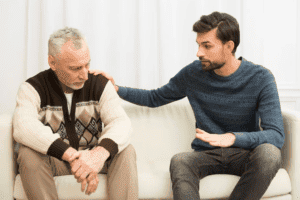 a young man condoling an elder man both sitting on a sofa